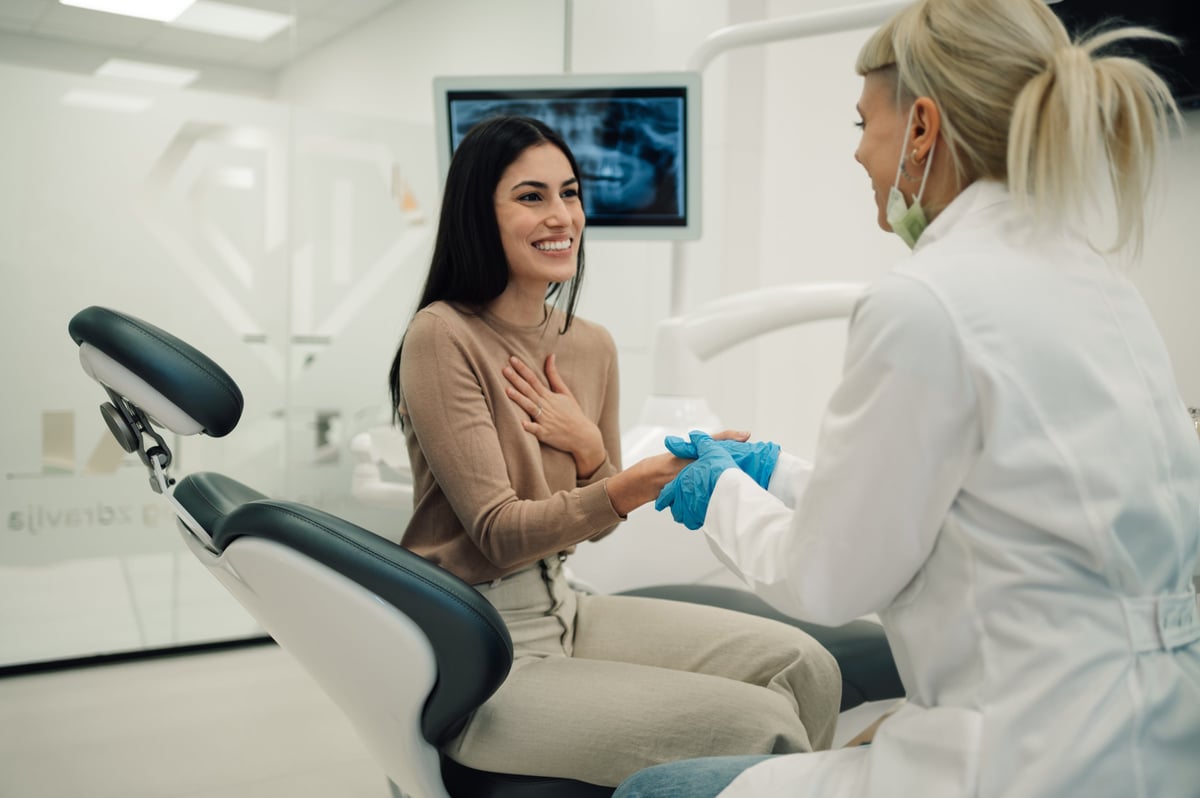 Female dentist holding hands of her relieved patient before starting a dental procedure in a modern dental clinic