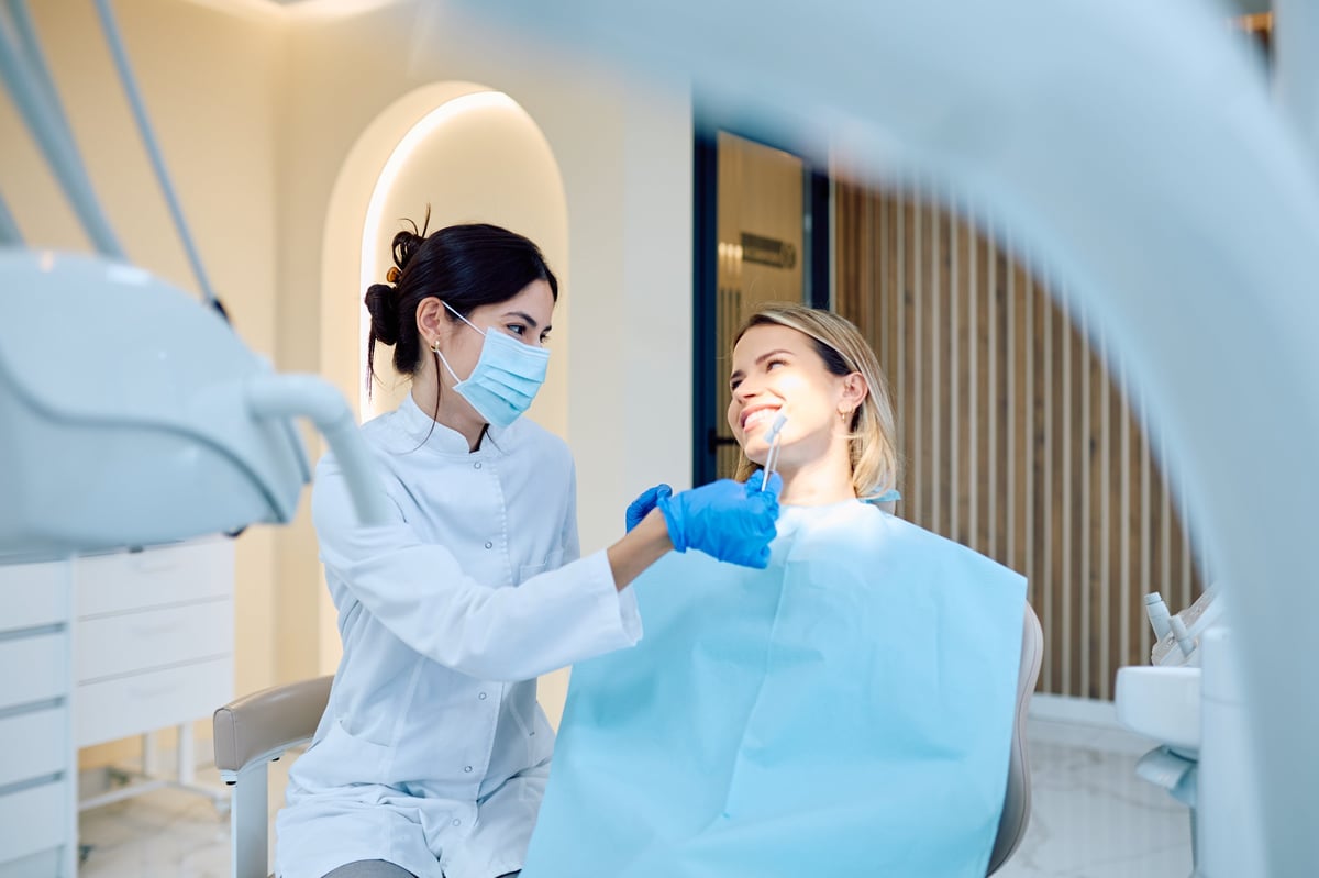 Dentist comparing teeth shade guide with client's healthy white smile in modern clinic