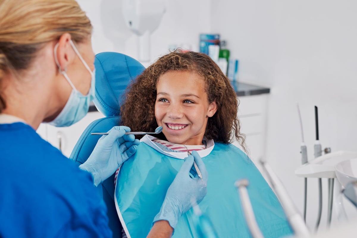 Smiling young girl in dental chair during check-up with dentist in modern clinic