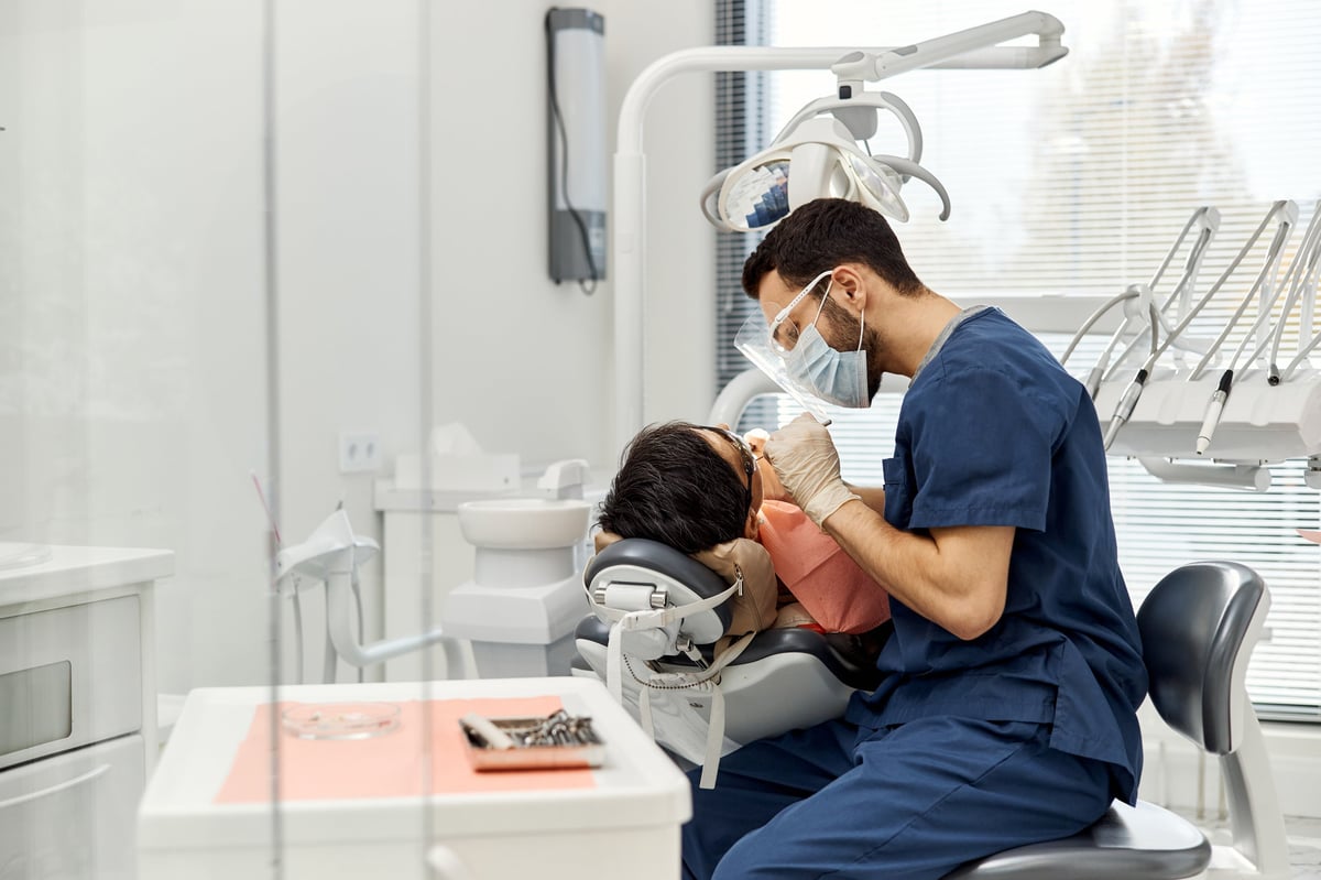 Middle Eastern male dentist examining patient in dental chair during routine checkup in modern dental office