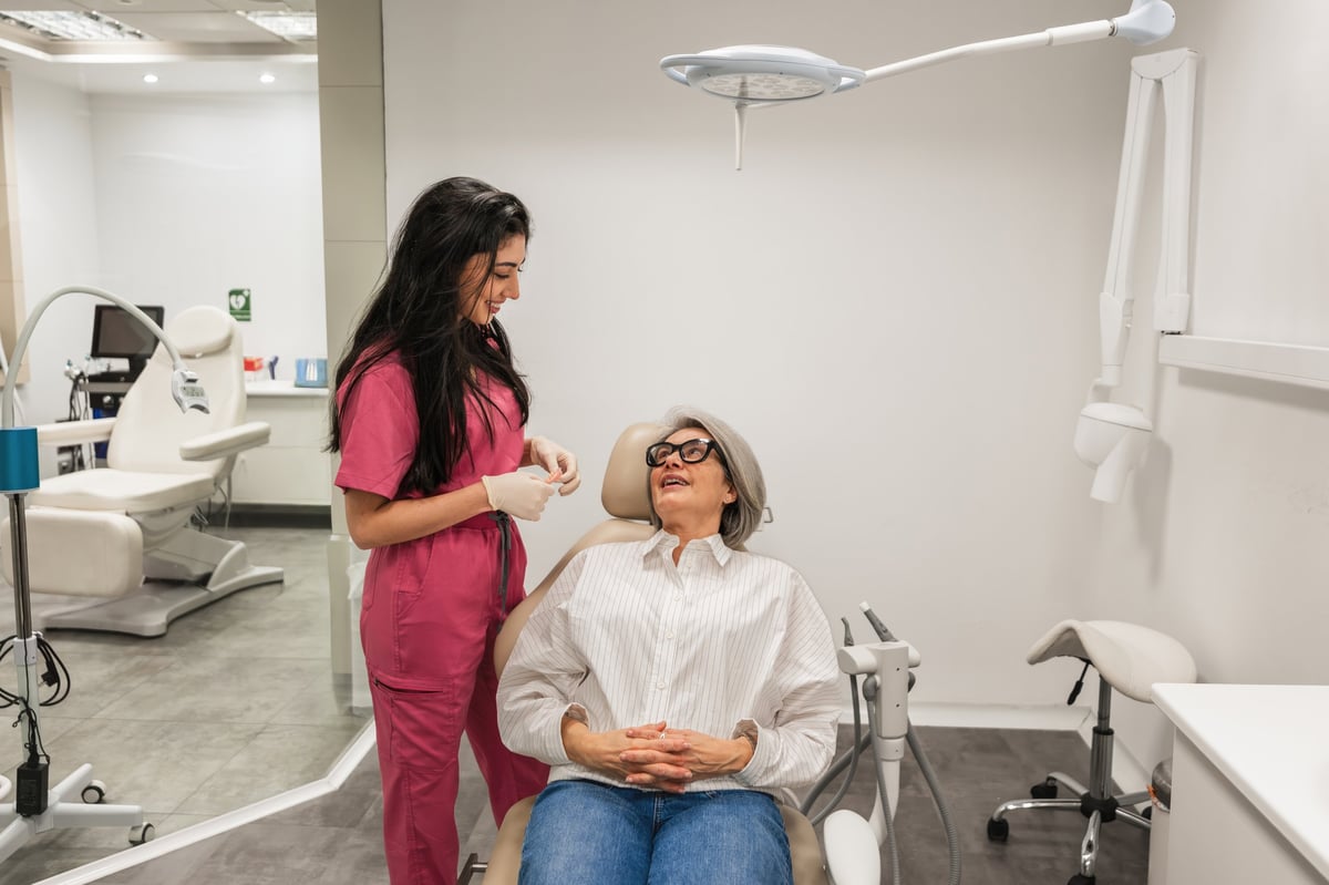 Female dentist talking with smiling senior patient during dental checkup in modern clinic
