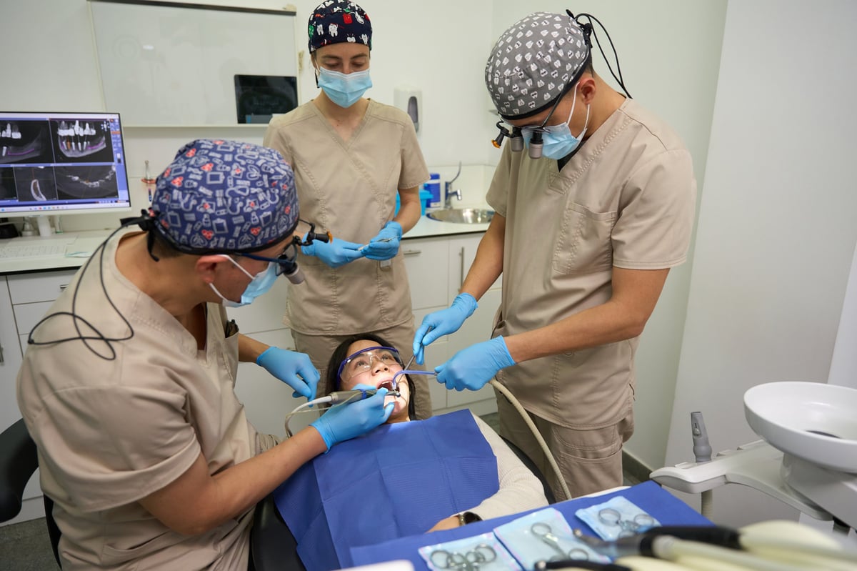 Dental surgeon, assistant, and orthodontist working together to provide gum care and teeth treatment for female patient in a modern dental office