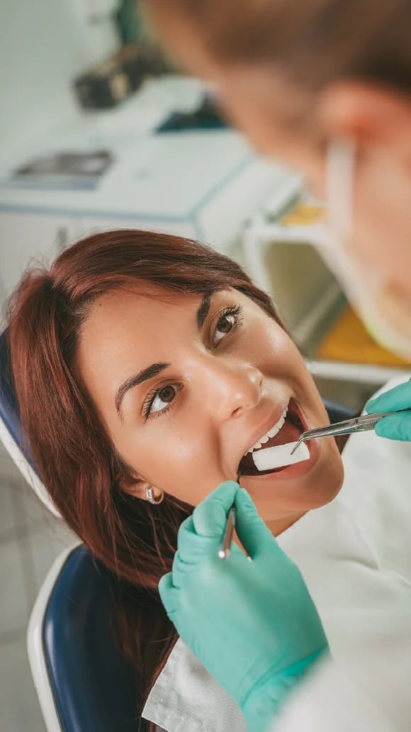 Woman receiving dental treatment from dentist wearing turquoise gloves in clinical setting