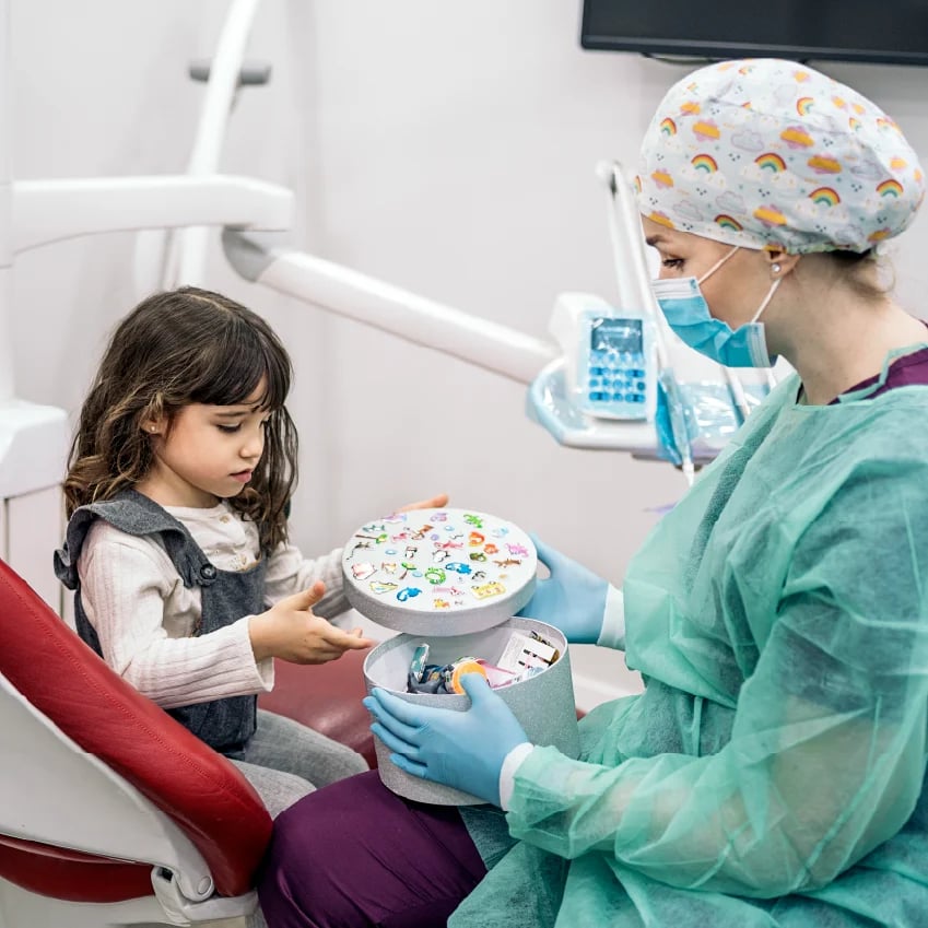 Young girl in dental chair receiving pediatric dental treatment from dentist, holding reward prize wheel