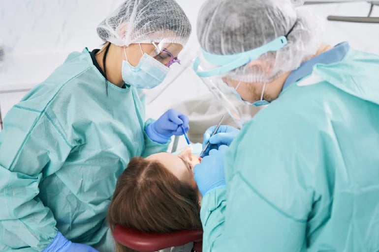 Two dental professionals in protective gear performing a dental procedure on a patient