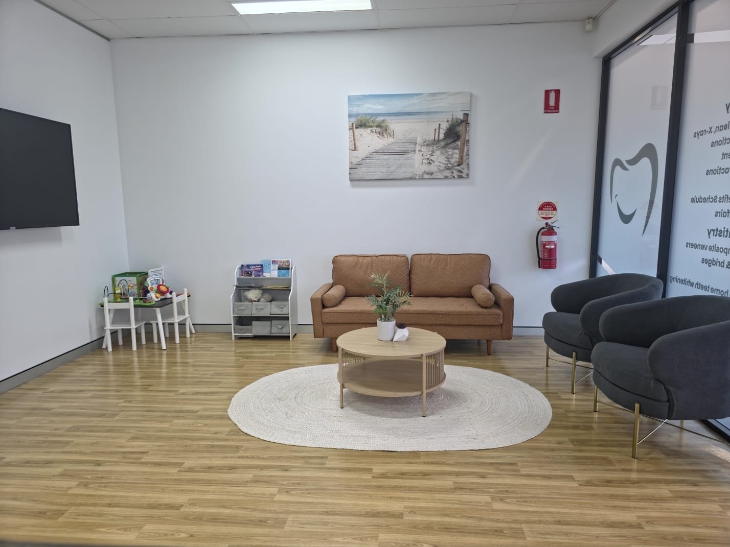 Modern waiting room with tan sofa, round wood table, black armchair, wooden flooring, and minimalist decor on white walls