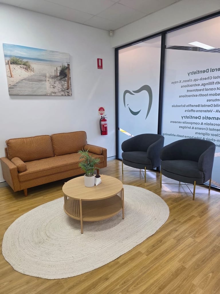 Modern office waiting room with tan leather sofa, wooden coffee table on oval rug, black accent chair, beach artwork, and glass partition wall